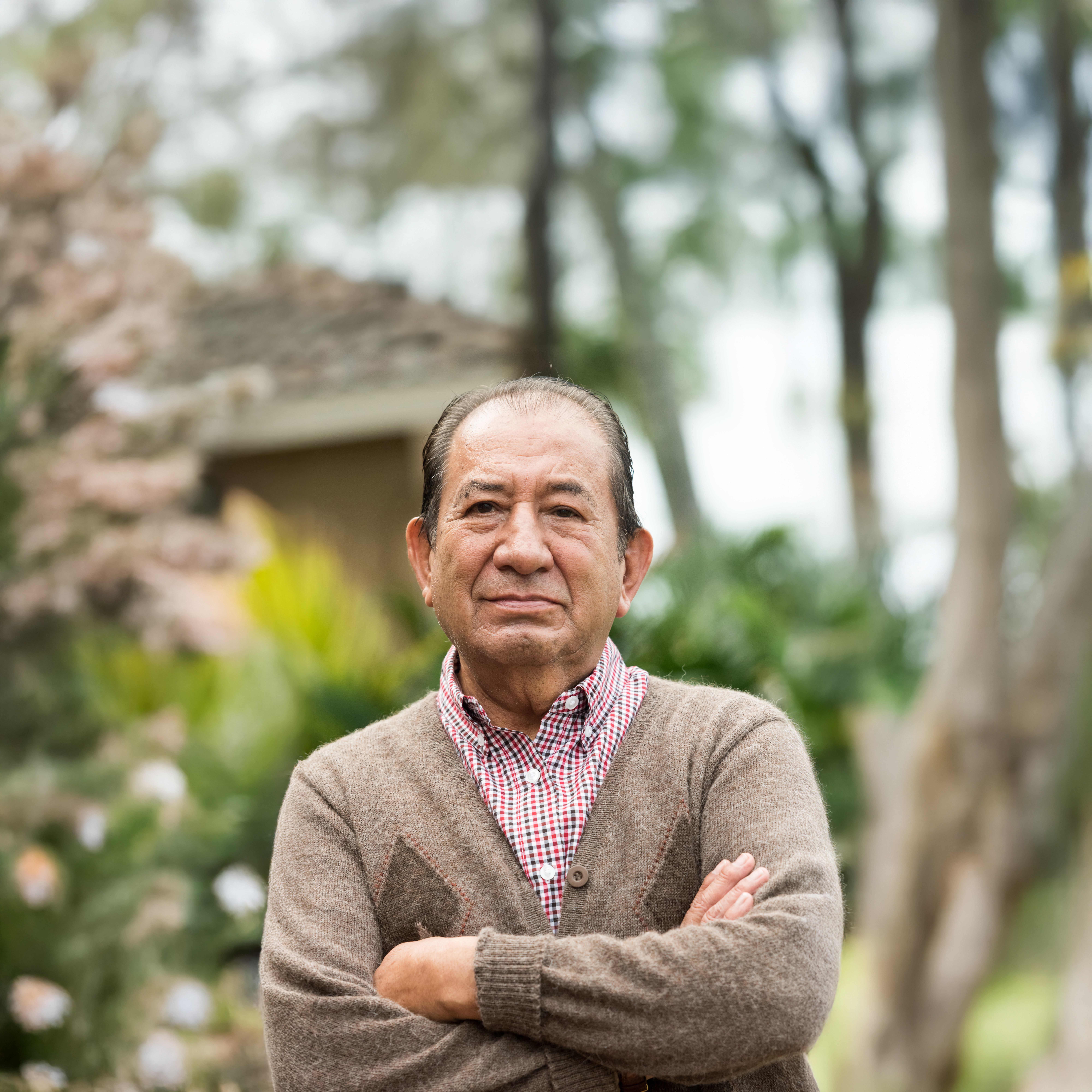 An older person looking forward with crossed arms and a content expression.