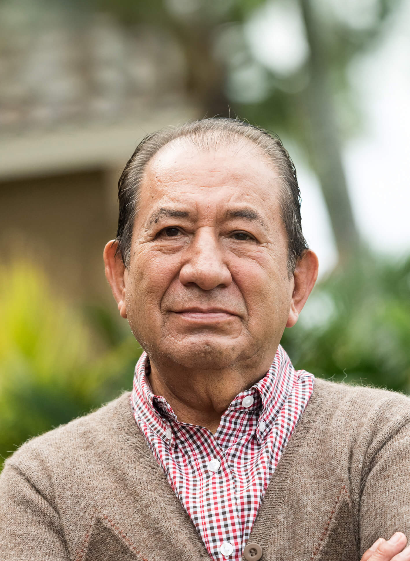 An older person looking forward with crossed arms and a content expression.