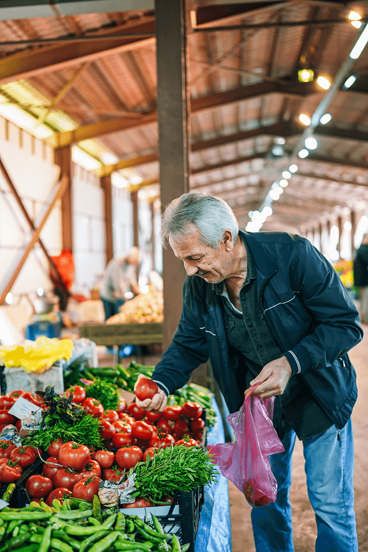 An upper middle-aged man selects a tomato from a vegetable stand in a market.